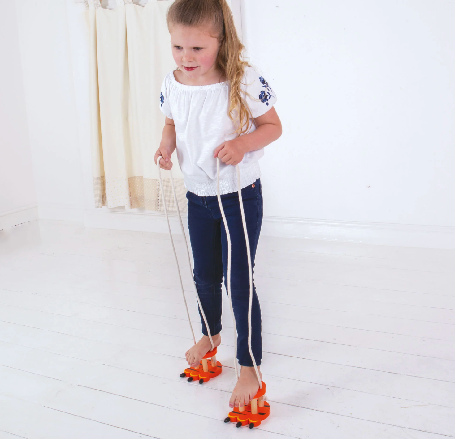 Child using a balance board on a white floor WOODEN FOOTWALKERS - 3 COLOURS | BIGJIGS