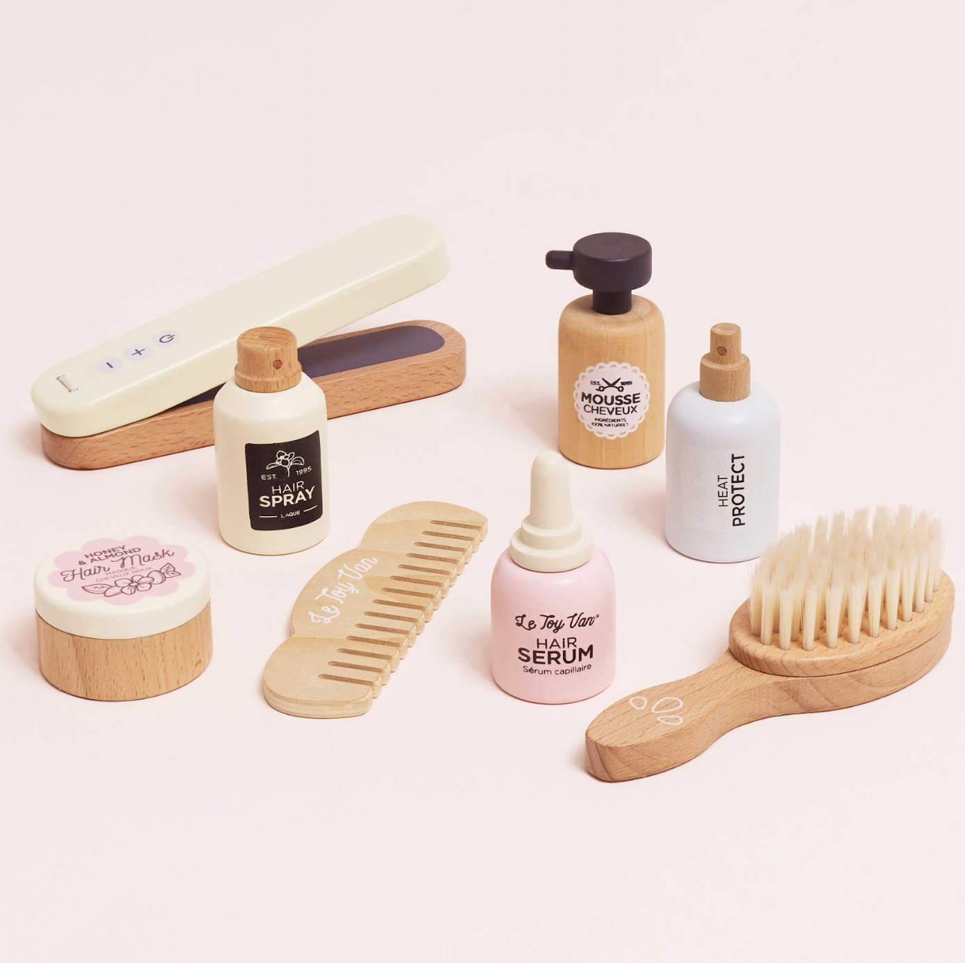 Collection of hair care products including bottles, a comb, and a brush on a light pink background. WOODEN HAIR STRAIGHTENERS & ACCESSORIES SET | LE TOY VAN