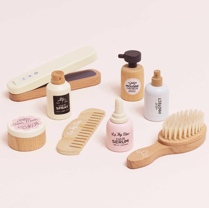 Collection of hair care products including bottles, a comb, and a brush on a light pink background. WOODEN HAIR STRAIGHTENERS & ACCESSORIES SET | LE TOY VAN