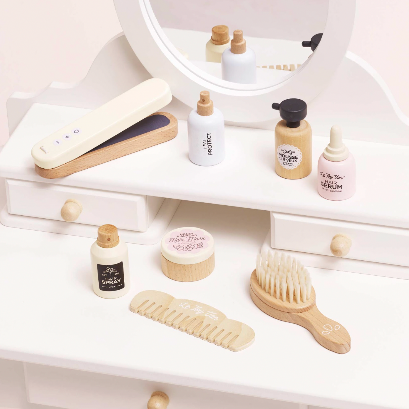 Cosmetic products and tools on a white shelf with a mirror in the background. WOODEN HAIR STRAIGHTENERS & ACCESSORIES SET | LE TOY VAN