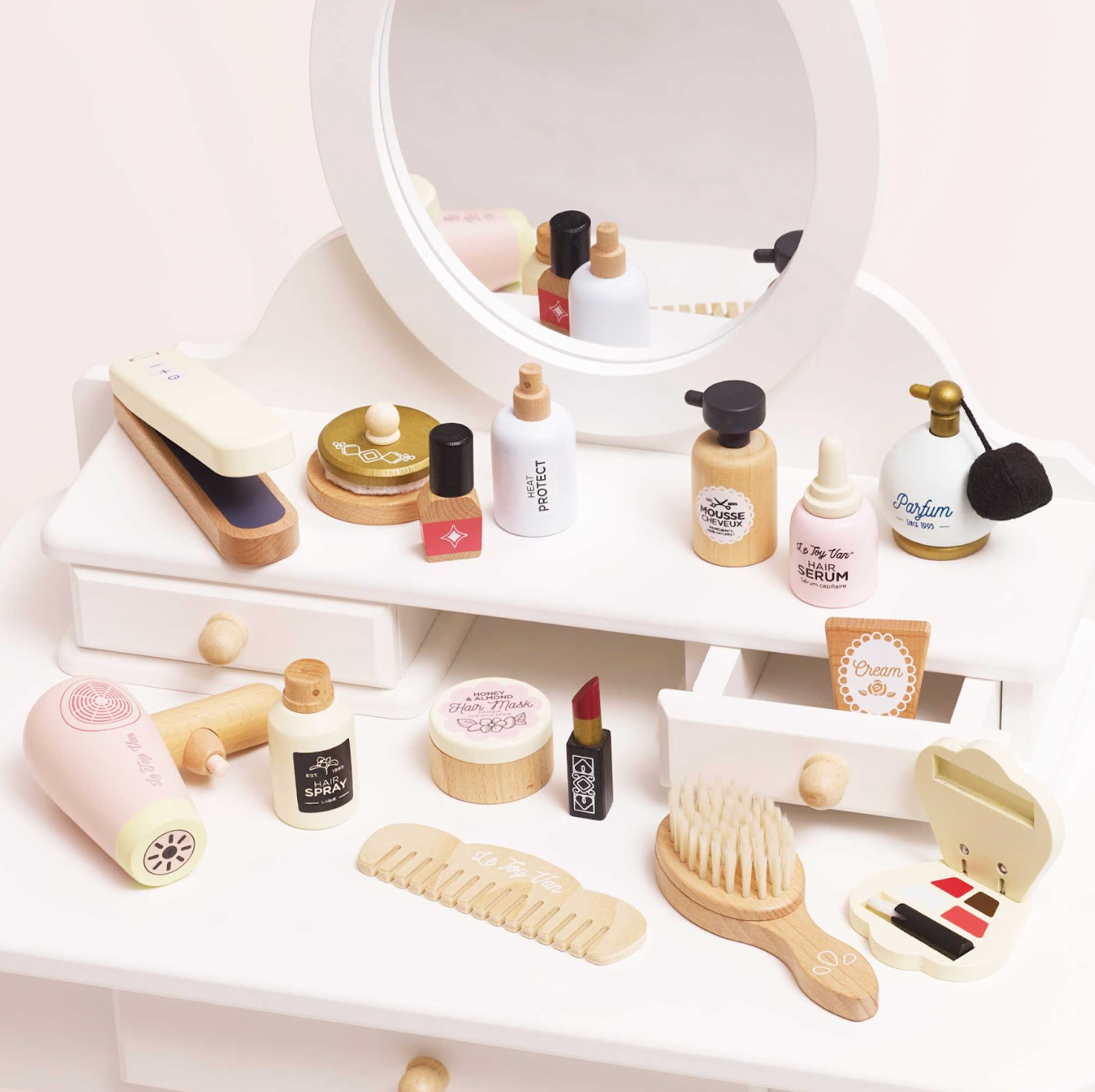 Collection of miniature beauty products and tools on a white surface with a mirror in the background. WOODEN HAIR STRAIGHTENERS & ACCESSORIES SET | LE TOY VAN