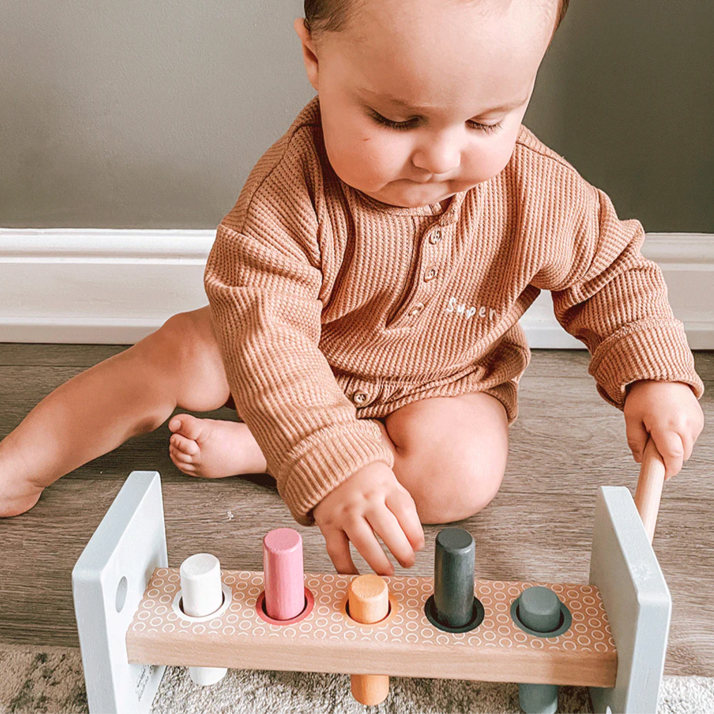 Child playing with a wooden toy on a wooden floor. WOODEN HAMMER BENCH | BIGJIGS