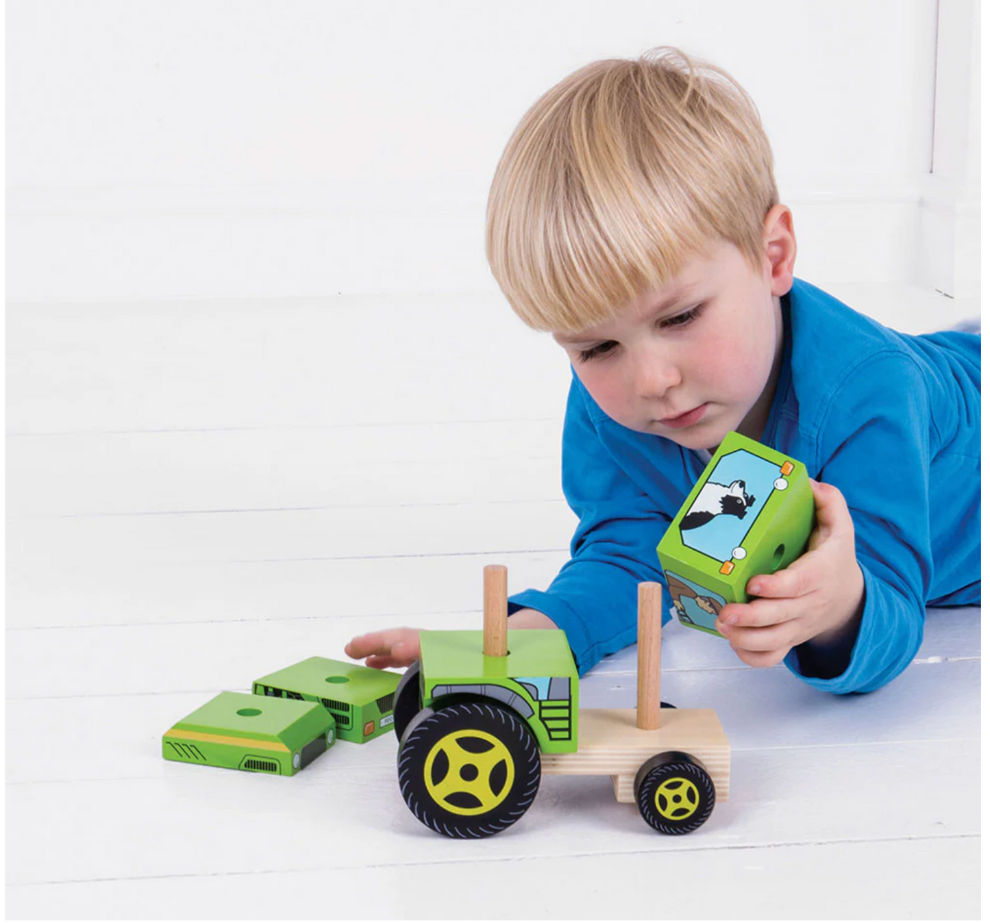 Child playing with a wooden toy tractor and green toy phone on a white surface WOODEN STACKING TRACTOR | BIGJIGS