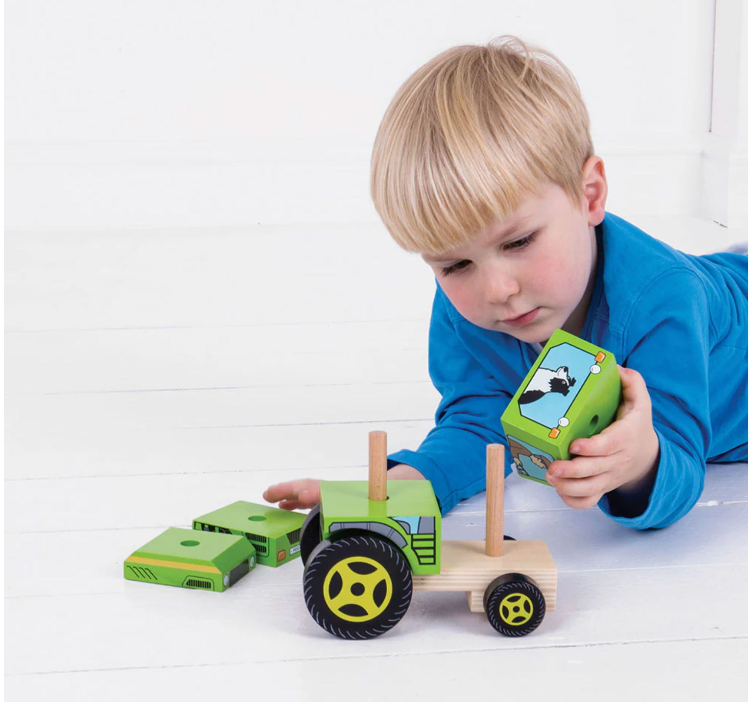 Child playing with a wooden toy tractor and green toy phone on a white surface WOODEN STACKING TRACTOR | BIGJIGS