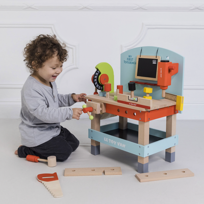 Child playing with a toy workbench set on a light gray floor. WOODEN TOOL BENCH | LE TOY VAN 