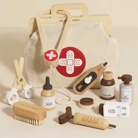 Collection of wooden and fabric items including a bag with a bandage design, bottles, and tools on a beige background. WOODEN TOY ANIMAL VET SET | LE TOY VAN