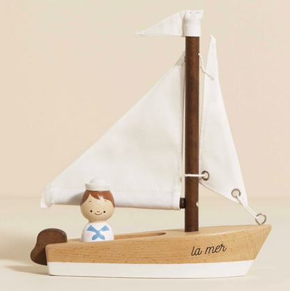 Wooden sailboat model with a small figure of a sailor on a beige background. WOODEN TOY SAILING BOAT & CAPTAIN | LE TOY VAN