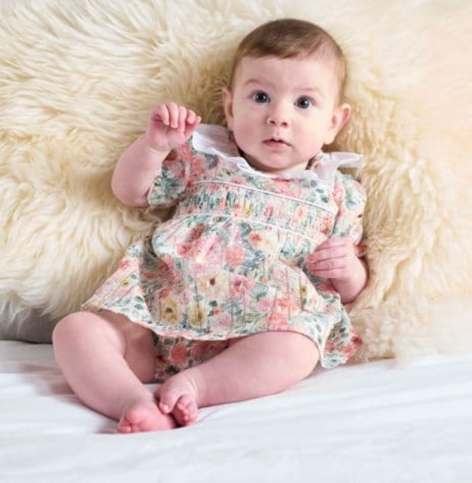 The Dandelion floral cotton summer smock dress displayed beautifully as a luxury traditional baby girl clothing gift.
